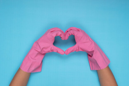woman wearing pink cleaning gloves on light blue background making heart sign with handの写真素材