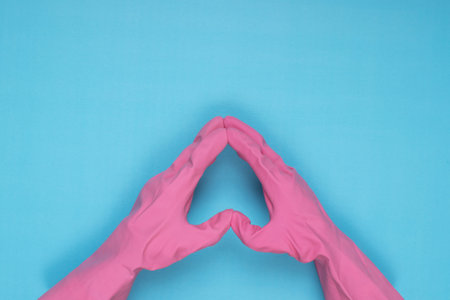 woman wearing pink cleaning gloves on light blue background making heart sign with handの写真素材