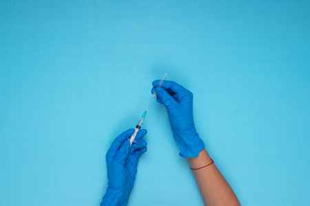 hand held needle with blue glove on light blue backgroundの写真素材