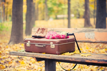 vintage suitcase, scarf, boots and umbrella on bench in autumn parkの写真素材