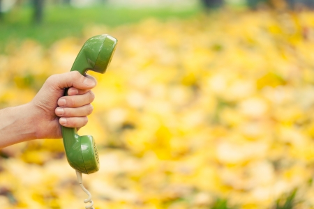 hand holding vintage phone receiver in autumn parkの写真素材