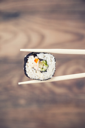Hand holding sushi roll using chopsticks on wooden backgroundの写真素材