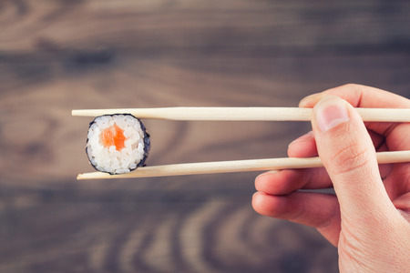 Hand holding sushi roll using chopsticks on wooden backgroundの写真素材