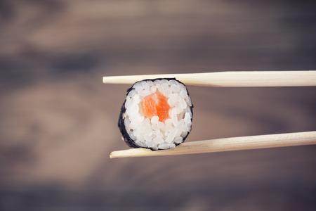 Hand holding sushi roll using chopsticks on wooden background