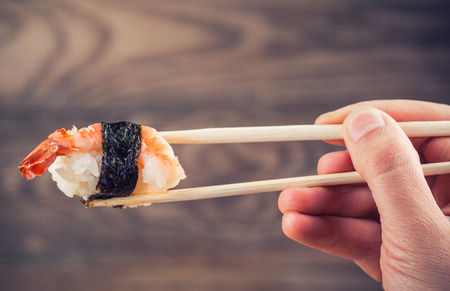 Hand holding sushi roll using chopsticks on wooden backgroundの写真素材