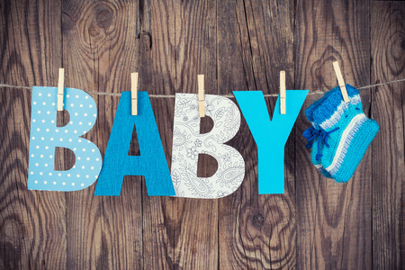 letters of word baby and knitted socks hanging on clothesline against wooden background