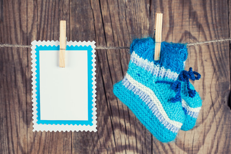 knitted baby socks and blank note hanging on clothesline against wooden backgroundの写真素材