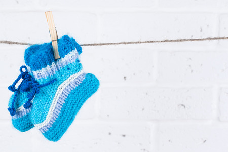 knitted baby socks hanging on clothesline against white brick wallの写真素材