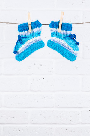 knitted baby socks hanging on clothesline against white brick wallの写真素材