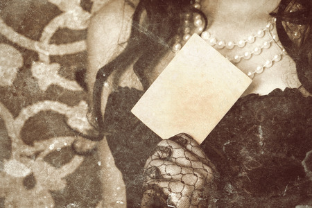 woman wearing black corset and pearls and holding a vintage paper sheet against retro backgroundの写真素材