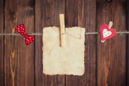 old paper sheet, red polka dot bow and small paper heart hanging on clothesline against wooden backgroundの写真素材
