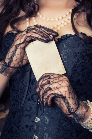 woman wearing black corset and pearls and holding a vintage paper sheet against retro backgroundの写真素材
