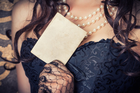woman wearing black corset and pearls and holding a vintage paper sheet against retro backgroundの写真素材
