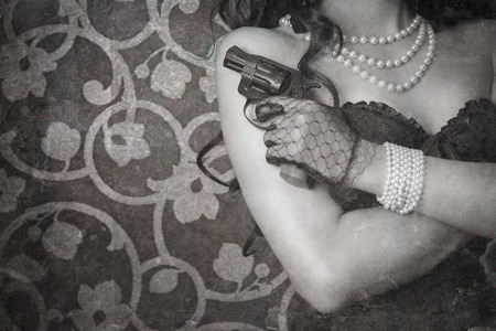 woman wearing black corset and pearls and holding a gun against retro backgroundの写真素材