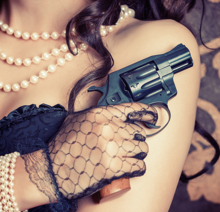 woman wearing black corset and pearls and holding a gun against retro backgroundの写真素材