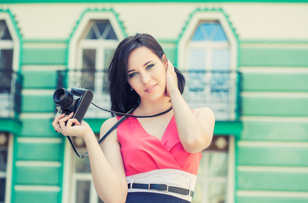 beautiful young woman taking photos with vintage camera on a city street