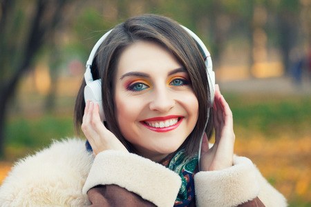 Young woman enjoying a music in the fall season. Autumn outdoor portrait.の写真素材