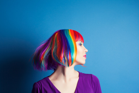 beautiful woman wearing colorful wig against blue backgroundの写真素材