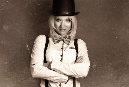 beautiful young woman wearing tophat, bow-tie and braces against grey background