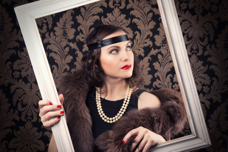 beautiful retro woman posing with white wooden frame against vintage wallpapersの写真素材