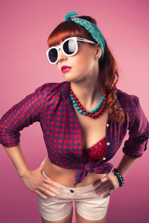 beautiful pin-up girl posing with white sunglasses against pink backgroundの写真素材