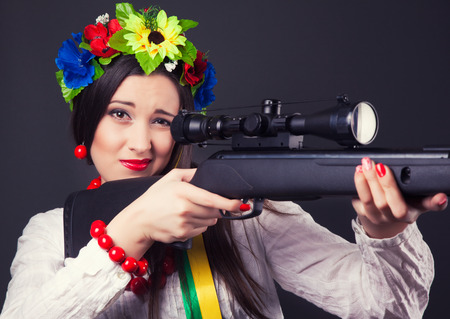 beautiful young woman wearing national ukrainian clothes and holding a rifleの写真素材