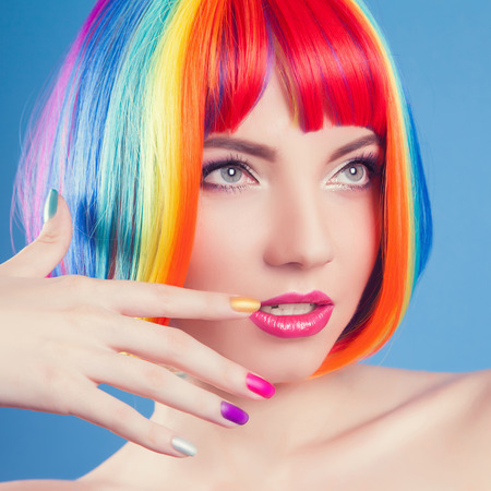 beautiful woman wearing colorful wig against blue backgroundの写真素材