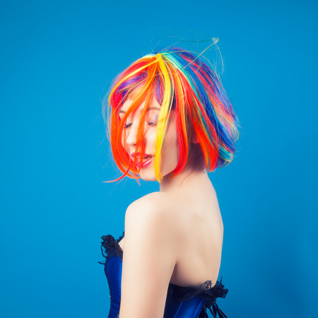 beautiful woman wearing colorful wig against blue backgroundの写真素材