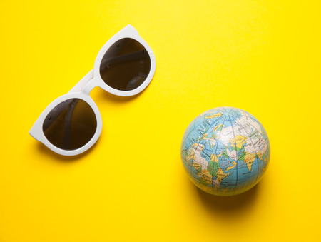 Stylish white sunglasses on yellow background with earth globeの写真素材