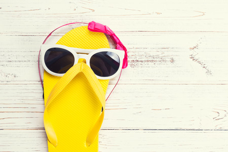Yellow flip flops and sunglasses on a white wooden backgroundの写真素材