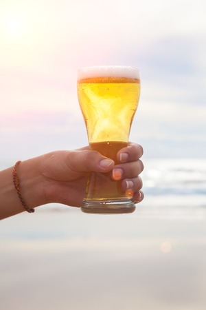Young woman hand holding a refreshing beer on the beachの写真素材
