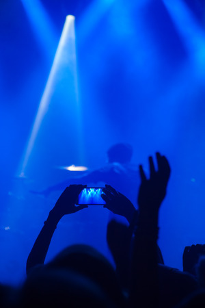 Silhouettes of people and musicians in big concert stage. Bright beautiful rays of lightの写真素材