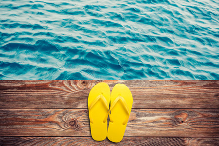 Yellow flip flops on a wooden background with water on back