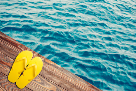 Yellow flip flops on a wooden background with water on backの写真素材