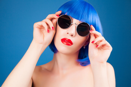 beautiful woman wearing colorful wig and silver sunglasses against blue backgroundの写真素材