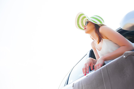 happy woman looks out the car window with suitcase in handsの写真素材