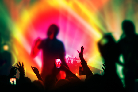 Silhouettes of people and musicians in big concert stage. Bright beautiful rays of lightの写真素材