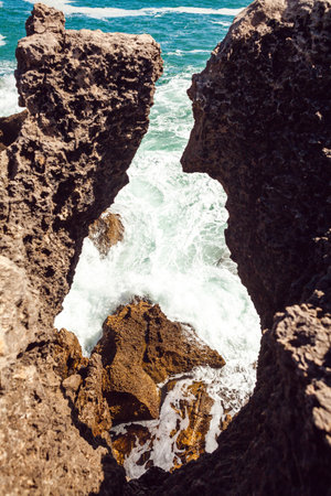 A peaceful ocean scene with shimmering blue water stretching to the horizon, rocky formations in the foreground, and a lone rock emerging from the waves, creating a tranquil and serene coastal atmosphereの写真素材
