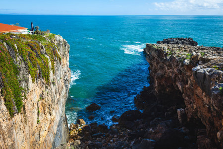 A dramatic coastal scene with steep cliffs covered in greenery, leading down to the deep blue ocean, with waves crashing against the rocky shore, creating a breathtaking and rugged seascape under a clear skyの写真素材