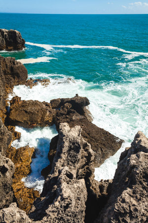 A peaceful ocean scene with shimmering blue water stretching to the horizon, rocky formations in the foreground, and a lone rock emerging from the waves, creating a tranquil and serene coastal atmosphereの写真素材
