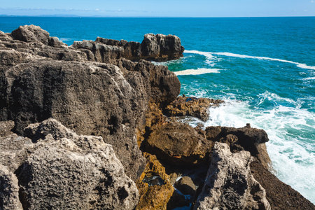 A peaceful ocean scene with shimmering blue water stretching to the horizon, rocky formations in the foreground, and a lone rock emerging from the waves, creating a tranquil and serene coastal atmosphereの写真素材
