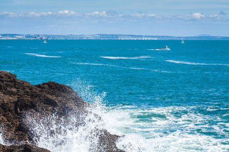 A peaceful ocean scene with shimmering blue water stretching to the horizon, rocky formations in the foreground, and a lone rock emerging from the waves, creating a tranquil and serene coastal atmosphereの写真素材