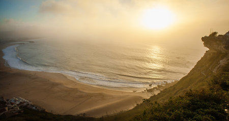 A peaceful, golden sunset over a wide sandy beach and calm ocean wavesの写真素材