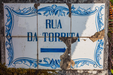 A weathered, decorative tile sign with blue lettering "Rua da Tordita" and a directional arrow, showing signs of age and damageの写真素材