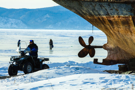 a quad biker on the coast at an old rusty fishing ship in winter