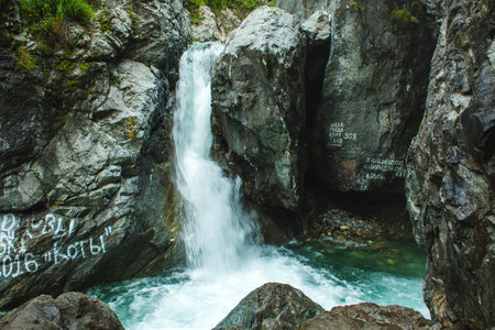 This image captures a small but vibrant waterfall cascading between rugged rocks into a pool of...