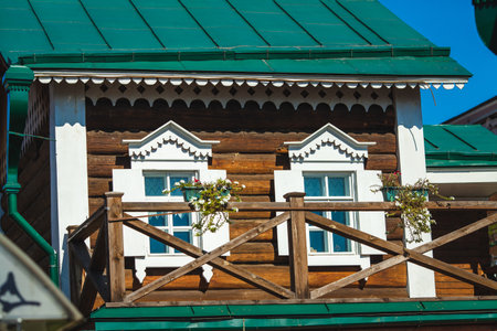 A close-up of a traditional wooden house with ornate white window frames and a green roof, adorned with flowersの写真素材