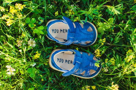 This photograph features a charming overhead shot of a pair of small blue sandals placed on a lush...