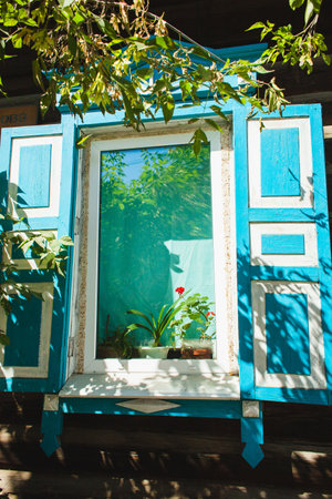 Charming wooden window with blue shutters, adorned with plants on a sunny day, surrounded by green foliageの写真素材