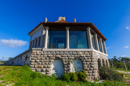 A stone and glass structure with a tiled roof stands on a grassy hill against a clear blue sky.の写真素材